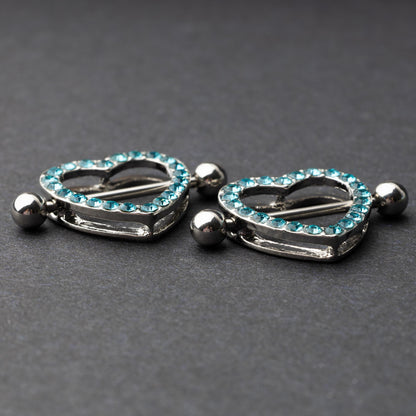 Two heart-shaped nipple barbells with silver metal and light blue gemstone accents, displayed on a dark background.