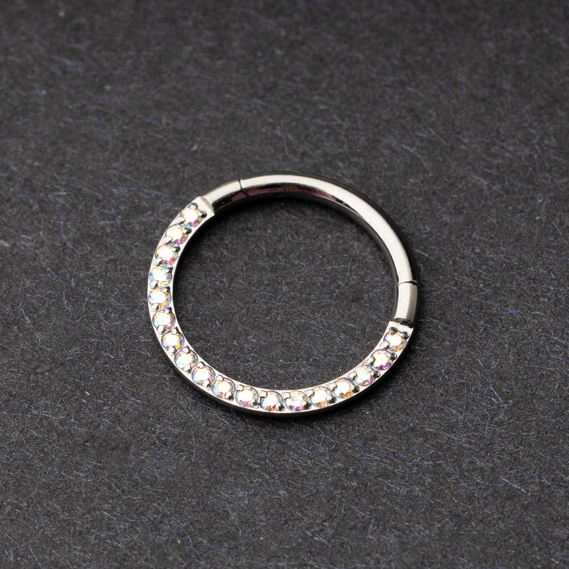 Titanium clicker ring with iridescent crystals, displayed on a dark background.