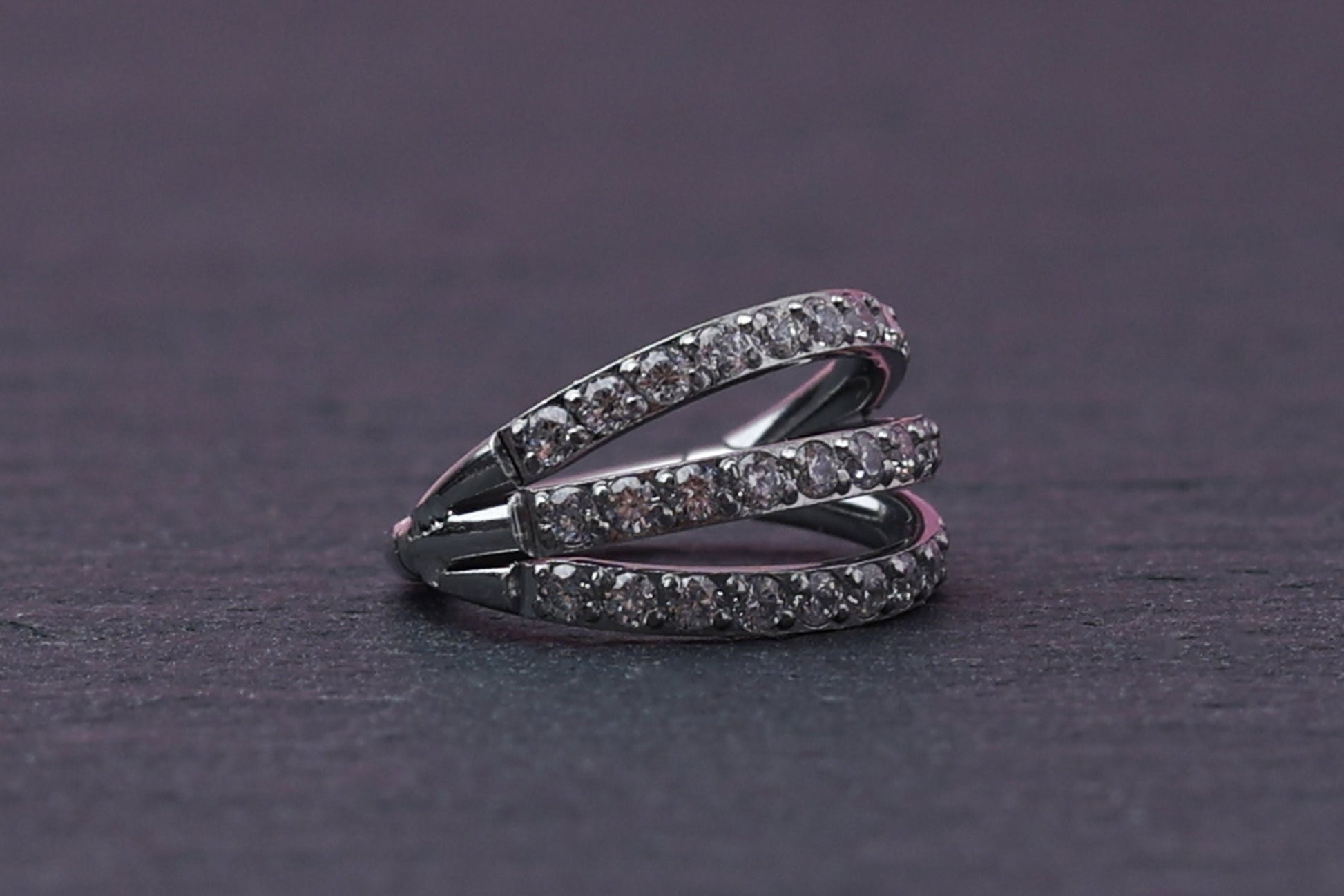 Triple-band clicker ring encrusted with cubic zirconia stones, displayed on a dark background, showcasing its elegant and sparkling design.