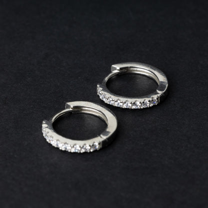 A pair of silver hoop earrings adorned with a row of sparkling cubic zirconia gems, displayed on a black background.