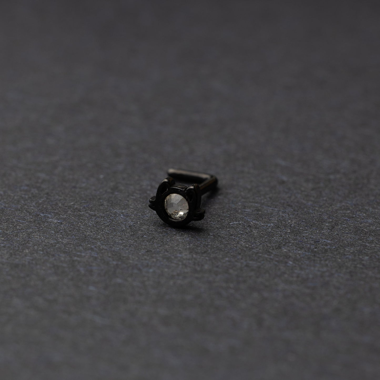 A black stud earring in the shape of a cat’s face with a bezel-set gemstone, displayed on a dark background.