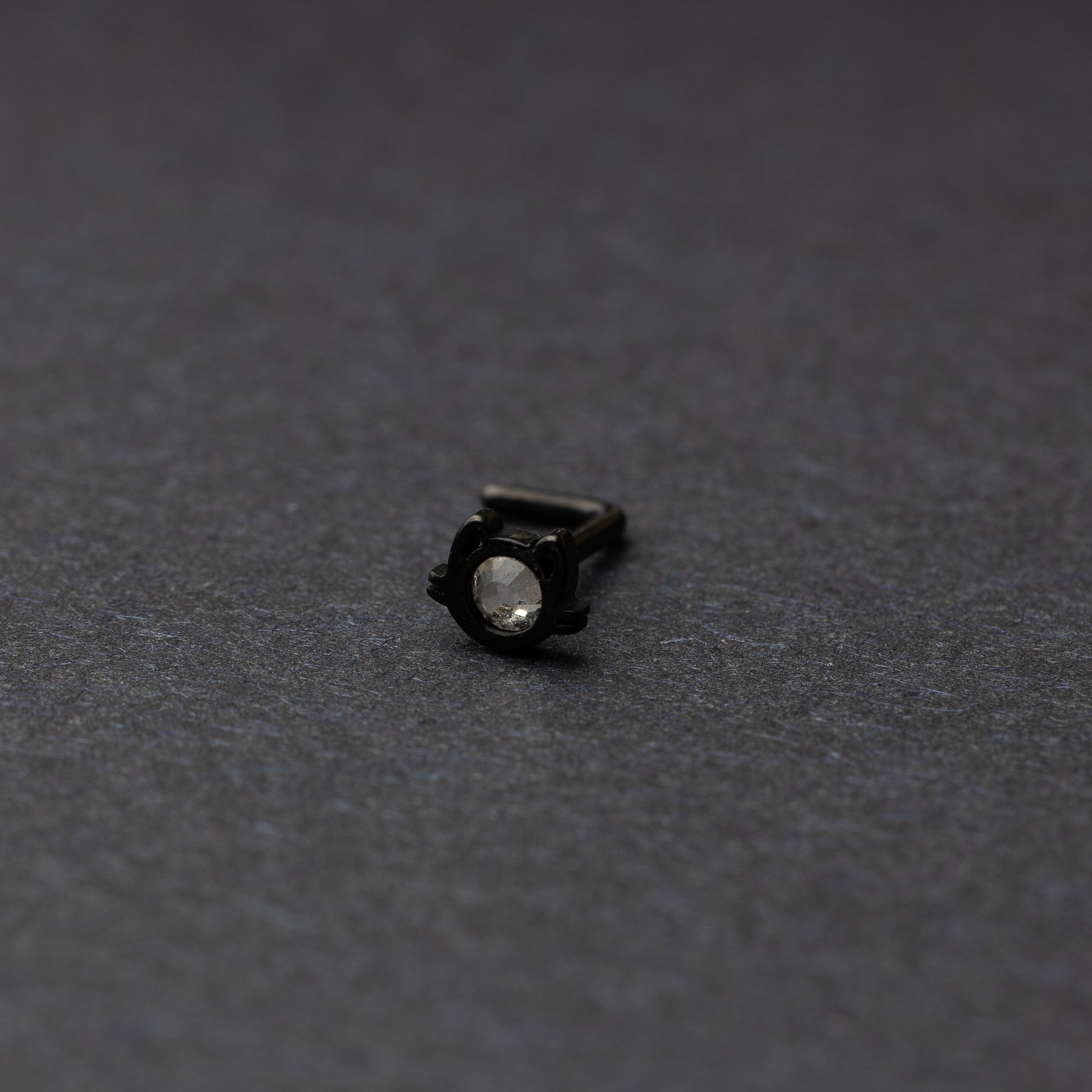 A black stud earring in the shape of a cat’s face with a bezel-set gemstone, displayed on a dark background.