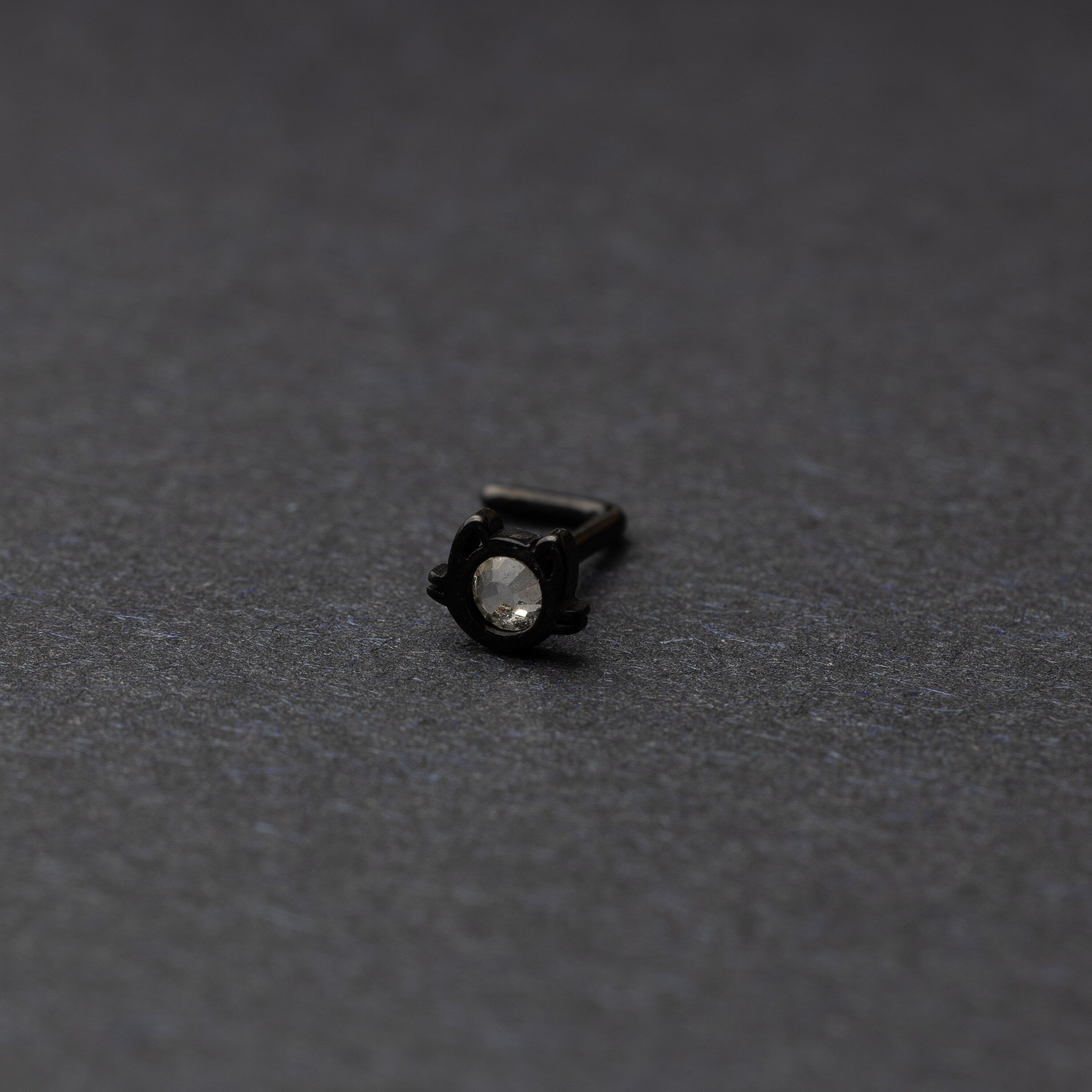 A black stud earring in the shape of a cat’s face with a bezel-set gemstone, displayed on a dark background.