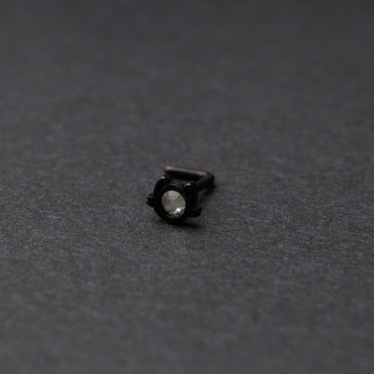 A black stud earring in the shape of a cat’s face with a bezel-set gemstone, displayed on a dark background.