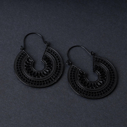 Pair of black hoop earrings with intricate cutout details and textured patterns, displayed on a dark background.