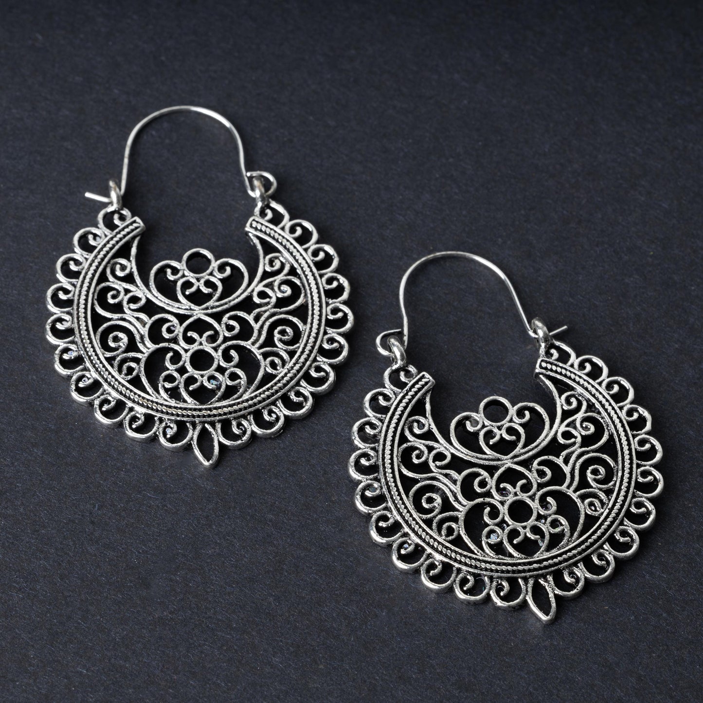 Pair of silver filigree hoop earrings with intricate scrollwork design, displayed on a dark background.