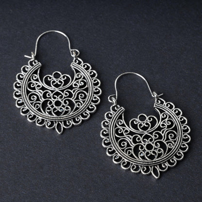 Pair of silver filigree hoop earrings with intricate scrollwork design, displayed on a dark background.