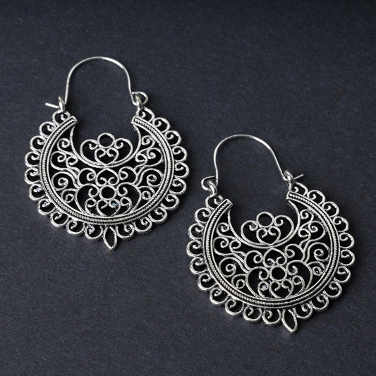 Pair of silver filigree hoop earrings with intricate scrollwork design, displayed on a dark background.