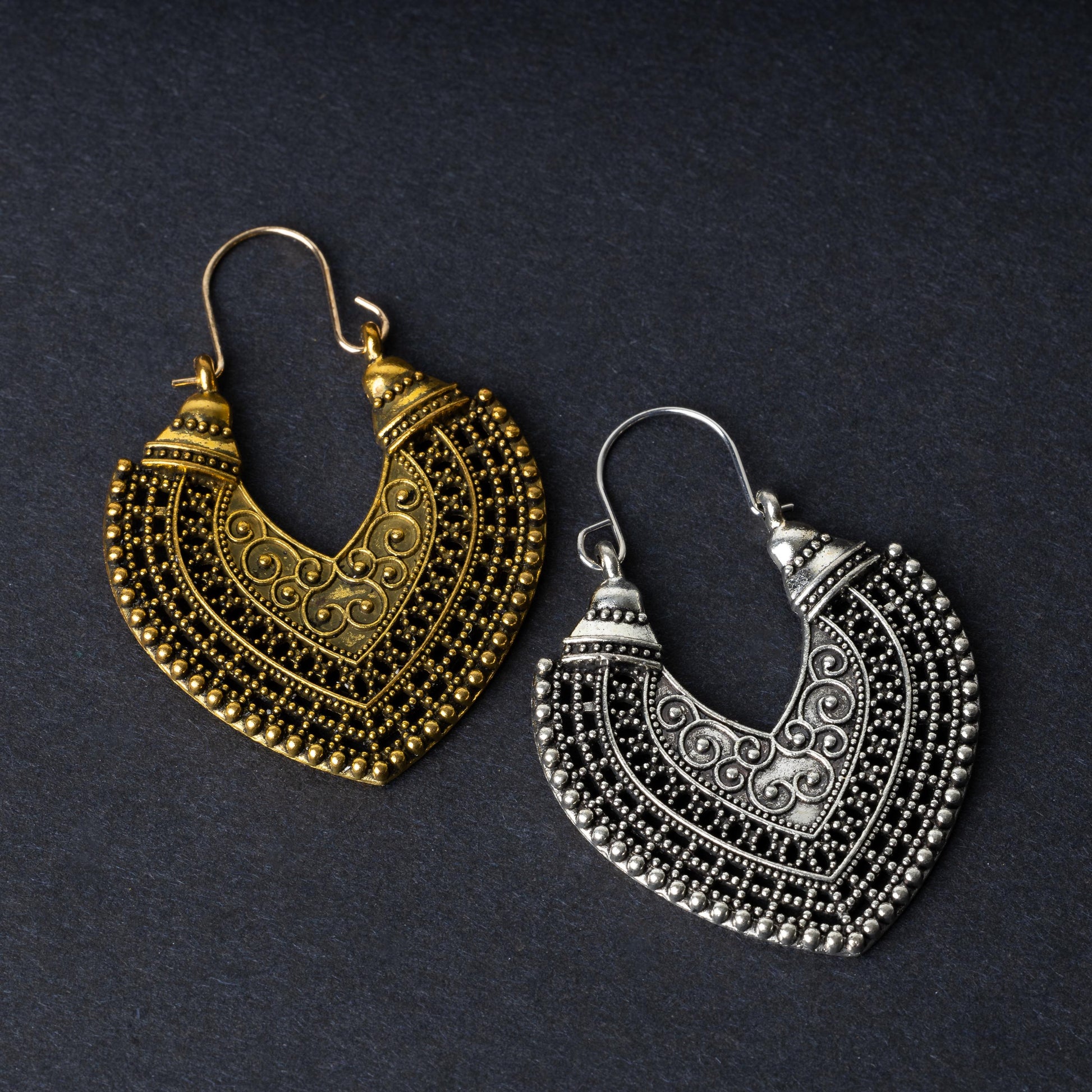 Pair of earrings in antique gold and silver finishes with intricate patterns and textured detailing, displayed on a dark background.
