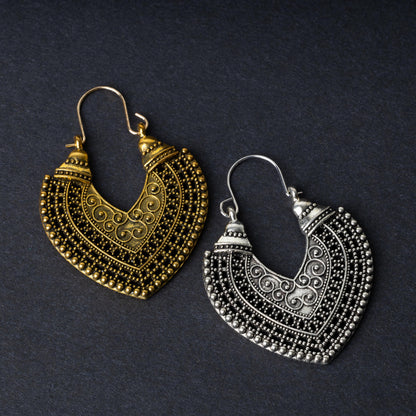 Pair of earrings in antique gold and silver finishes with intricate patterns and textured detailing, displayed on a dark background.