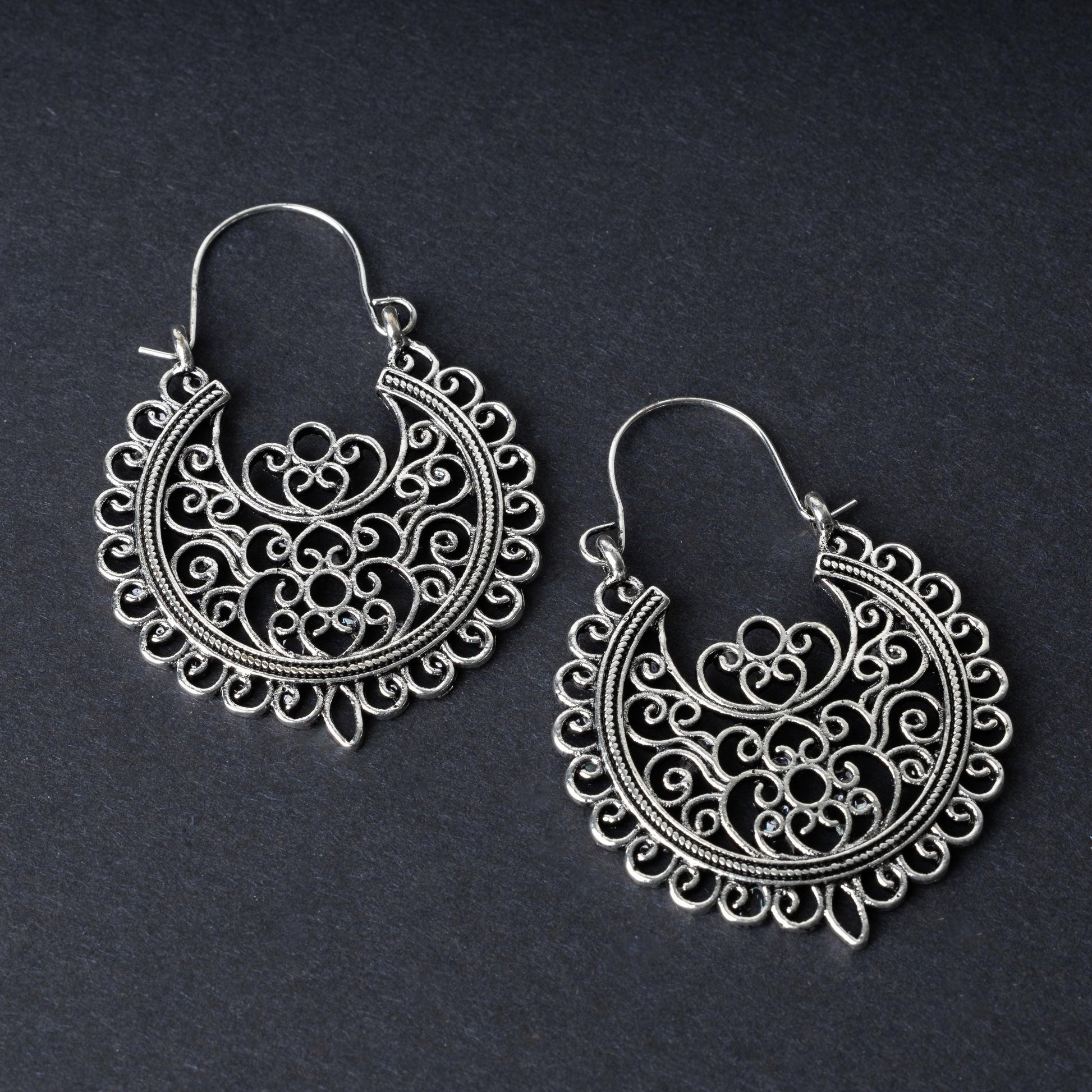Pair of silver filigree hoop earrings with intricate scrollwork design, displayed on a dark background.