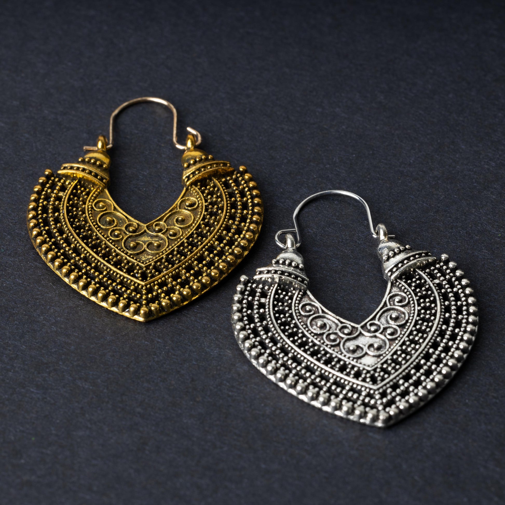 Pair of earrings in antique gold and silver finishes with intricate patterns and textured detailing, displayed on a dark background.