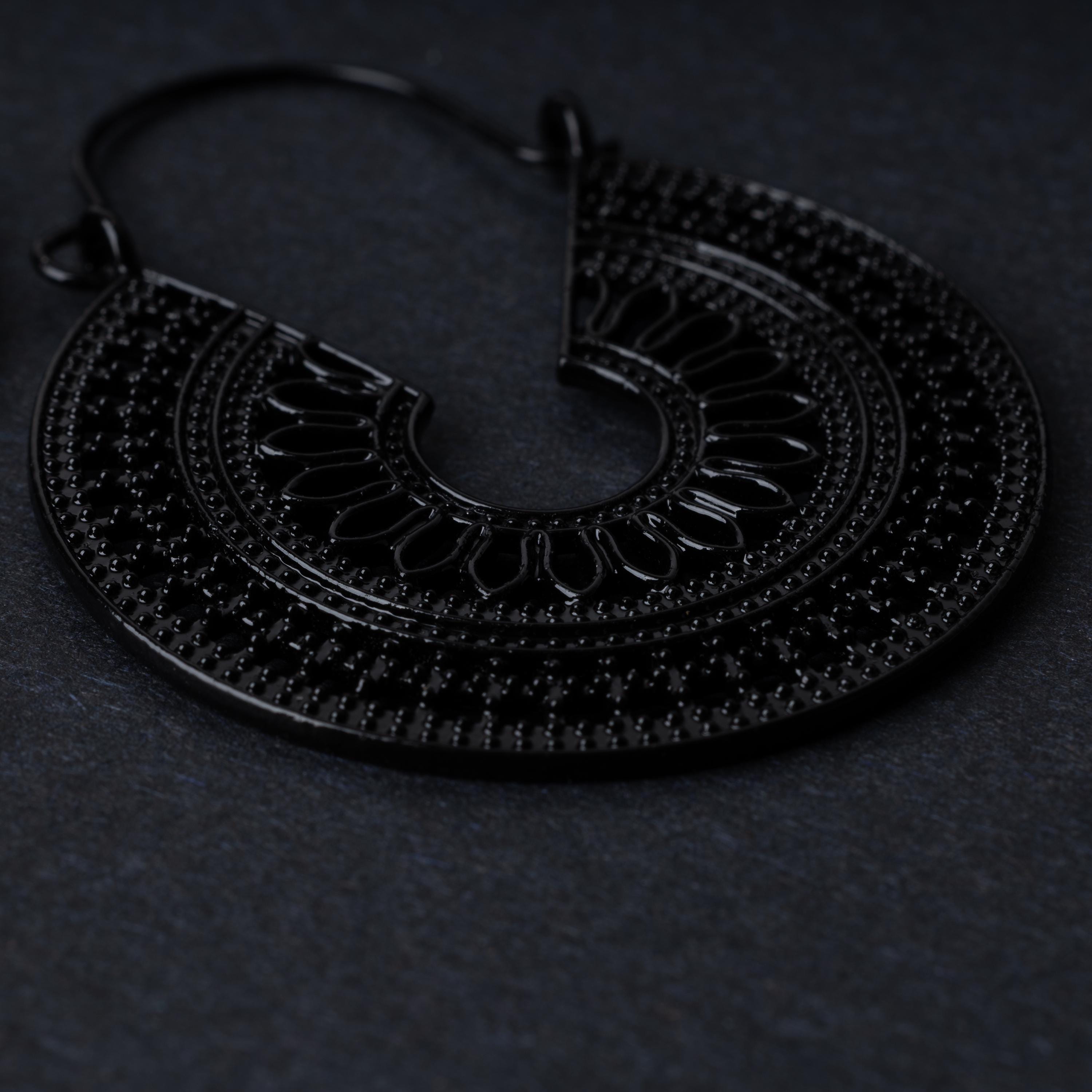 Close up of a single mandala earring in black, displayed on a black background.
