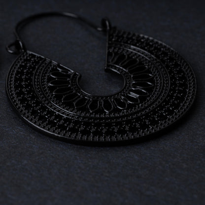 Close up of a single mandala earring in black, displayed on a black background.