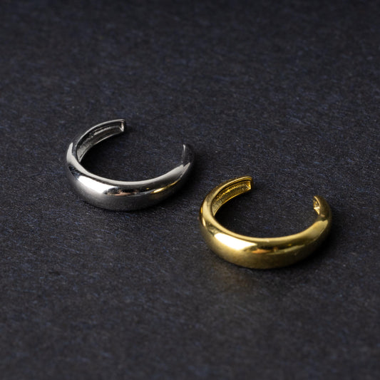 Bold ear cuffs in silver and gold finishes with a smooth, domed design, displayed on a dark background.