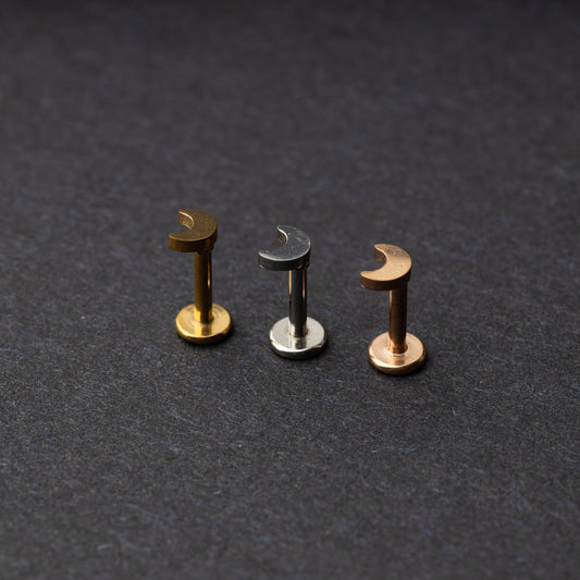 Gold, silver, and rose gold crescent moon labret studs displayed on a dark background.