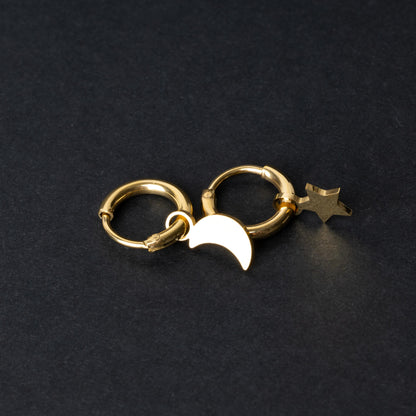 Gold huggie hoop earrings featuring a crescent moon charm on one hoop and a star charm on the other, displayed on a dark background.