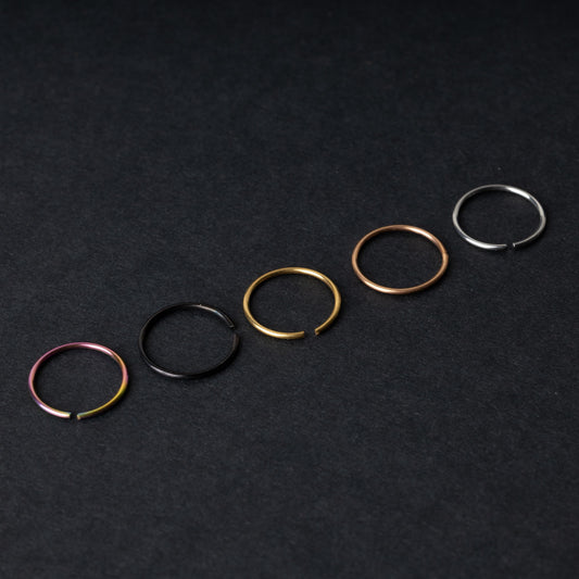 Five thin seamless hoops in rainbow, black, gold, rose gold, and silver finishes, displayed on a dark background.
