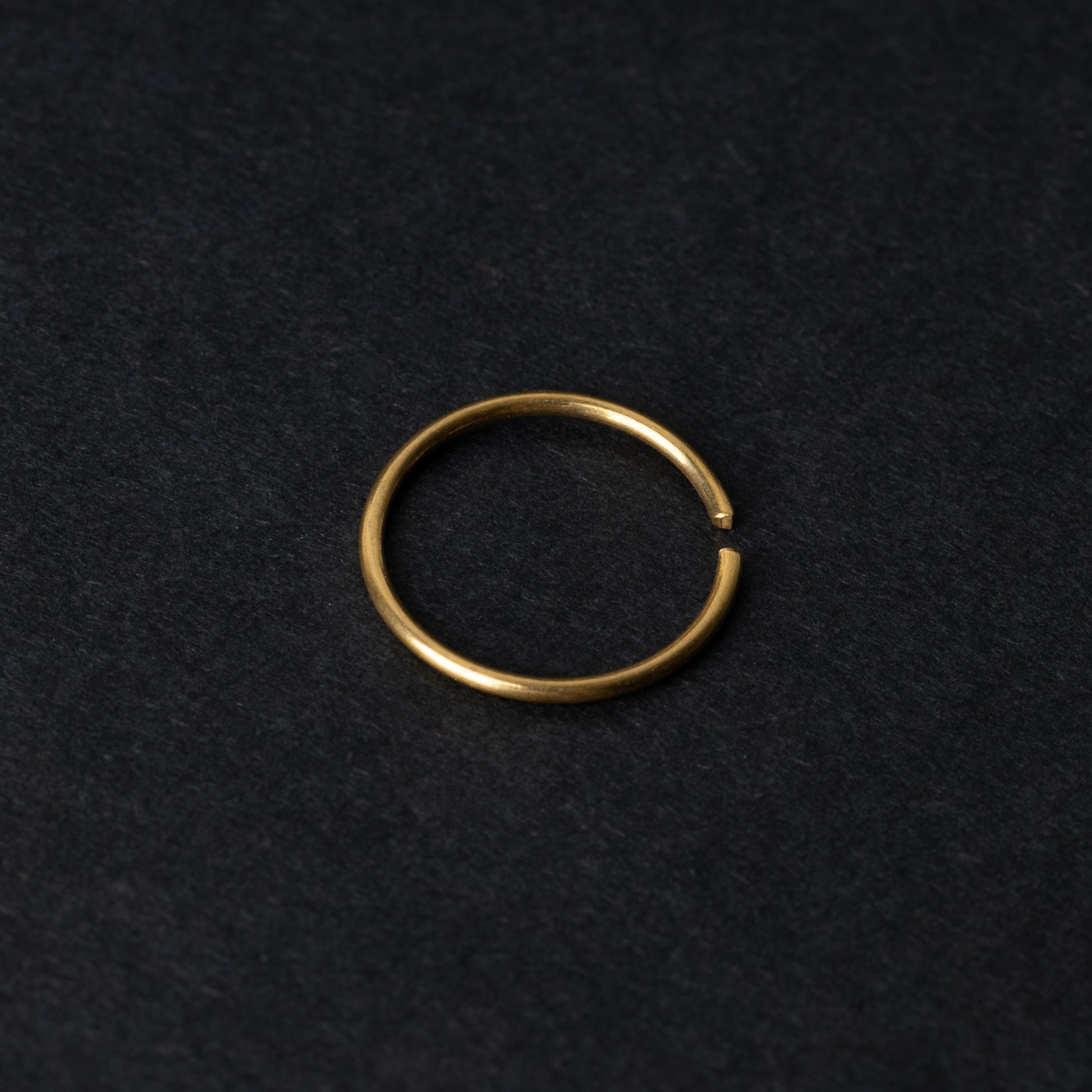 A single thin gold seamless hoop with a polished finish, displayed on a dark background.
