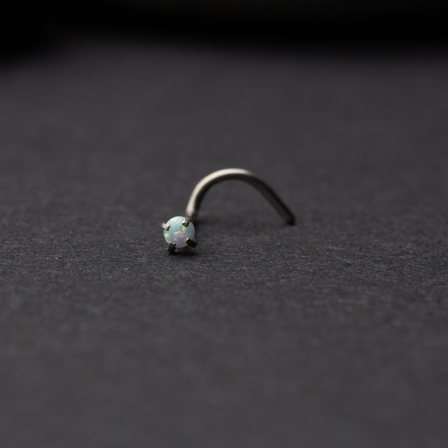 Single opalescent nose screw with a prong setting, displayed on a dark background.
