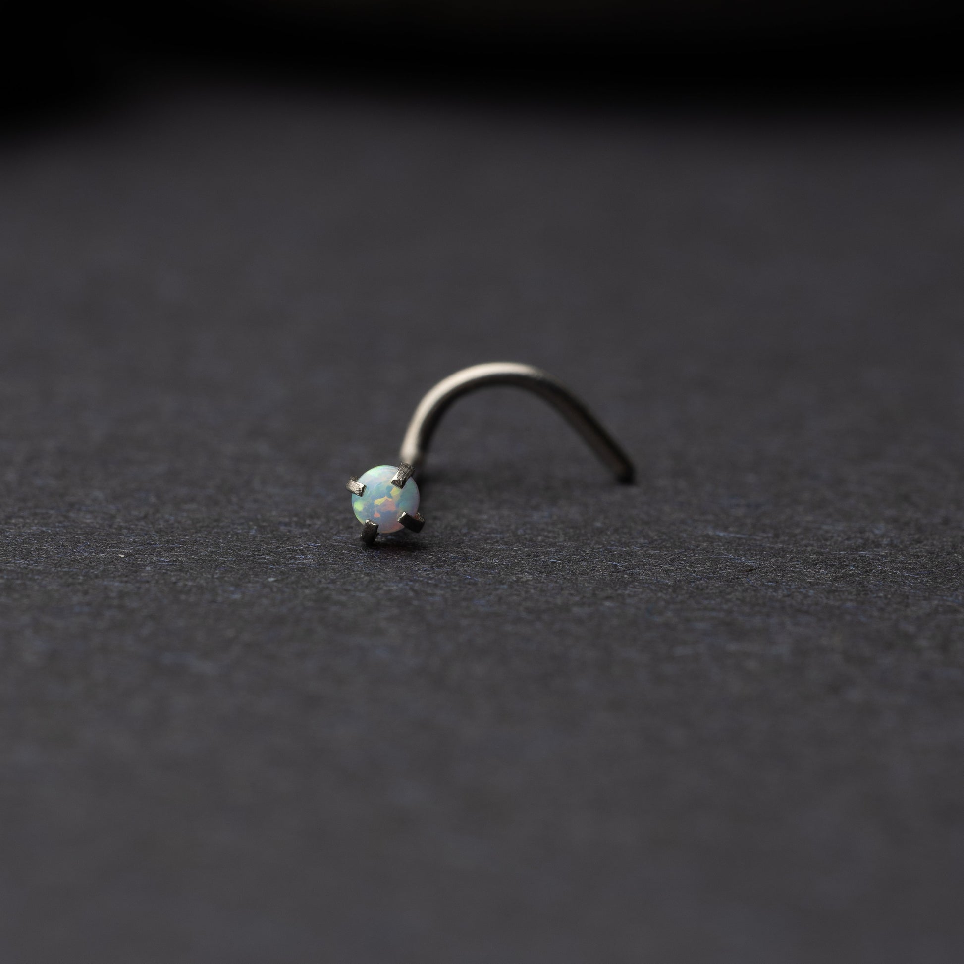 Single opalescent nose screw with a prong setting, displayed on a dark background.