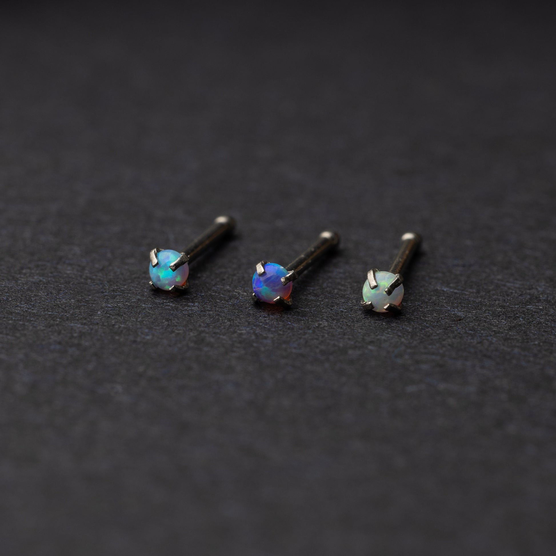 Three opalescent nose studs with prong settings, displayed on a dark background.
