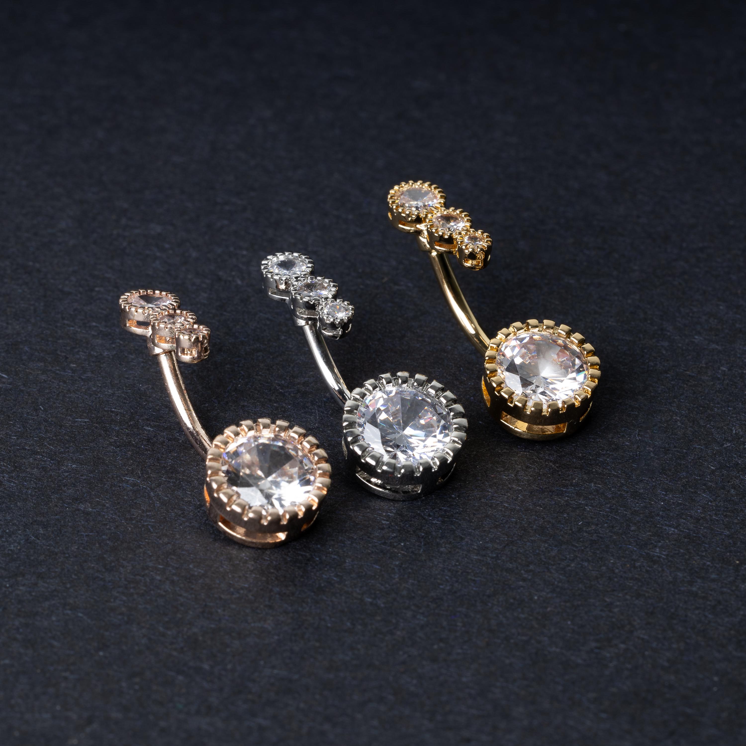 Double-jeweled belly rings in gold, silver, and rose gold finishes with large and small crystal accents, displayed on a dark background.