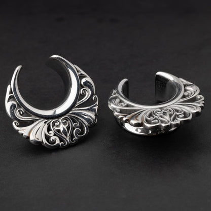 Pair of silver saddle tunnels with swirling decorative patterns for stretched ears.