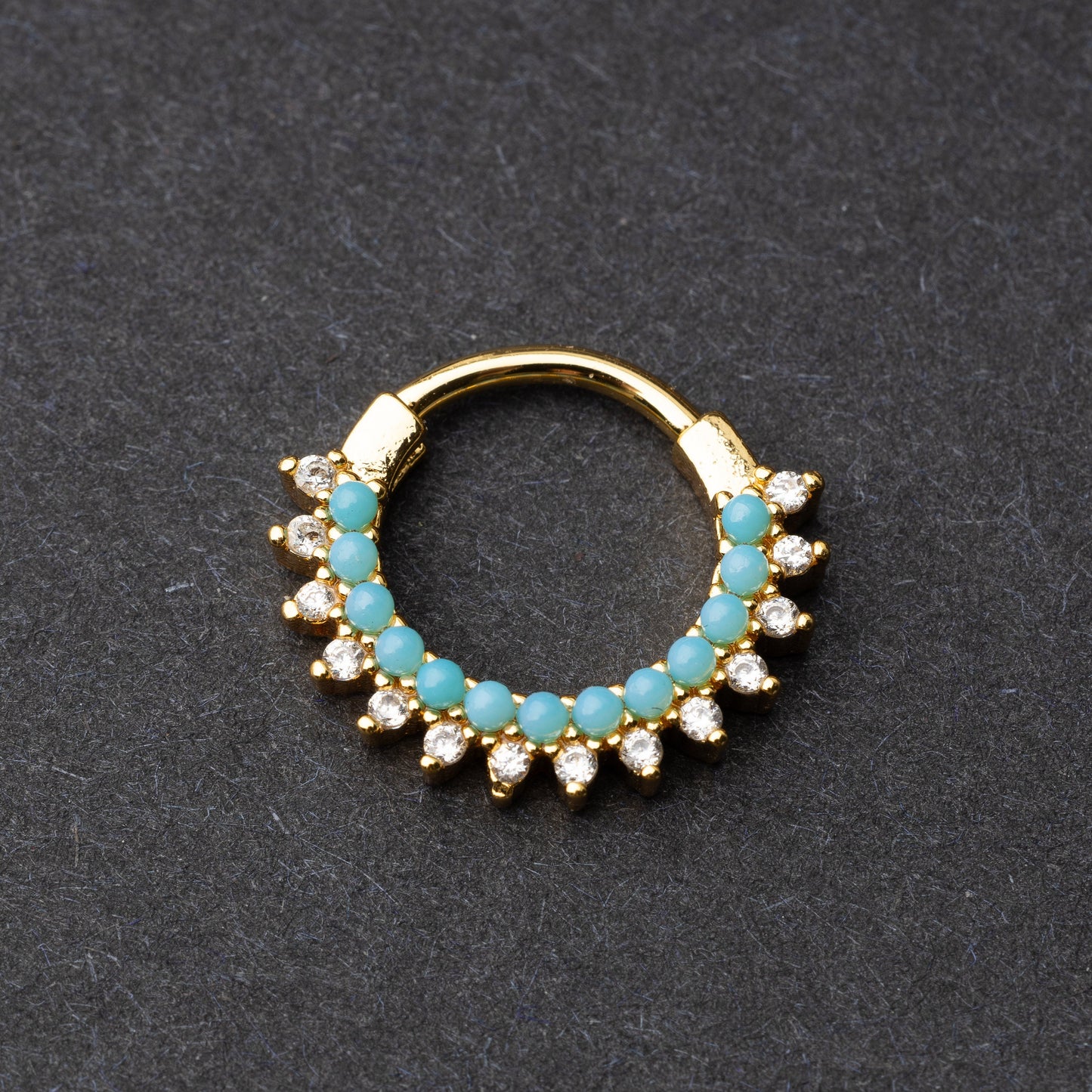 Gold-tone septum clicker with turquoise beads and cubic zirconia stones arranged in an elegant pattern, displayed on a dark background.