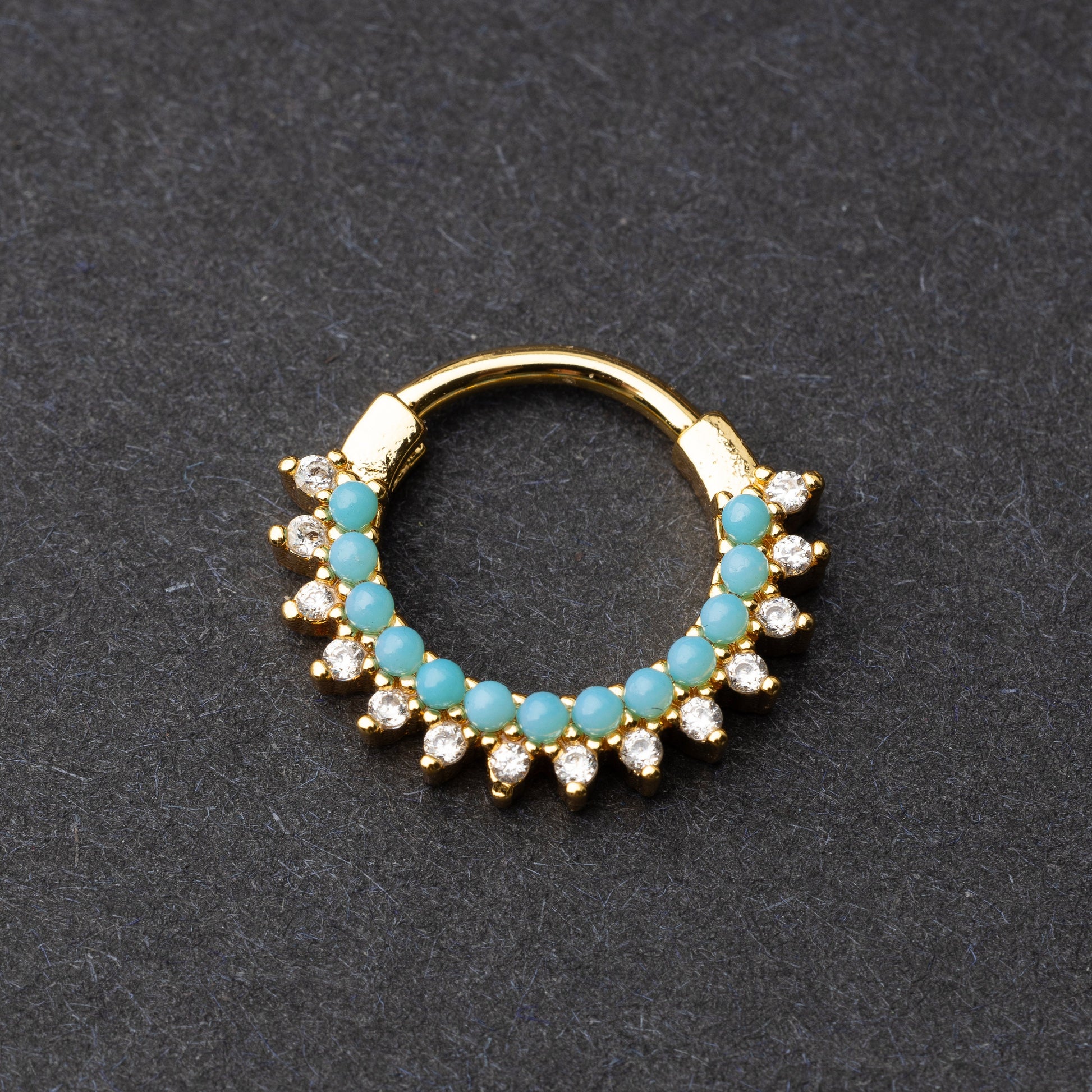 Gold-tone septum clicker with turquoise beads and cubic zirconia stones arranged in an elegant pattern, displayed on a dark background.