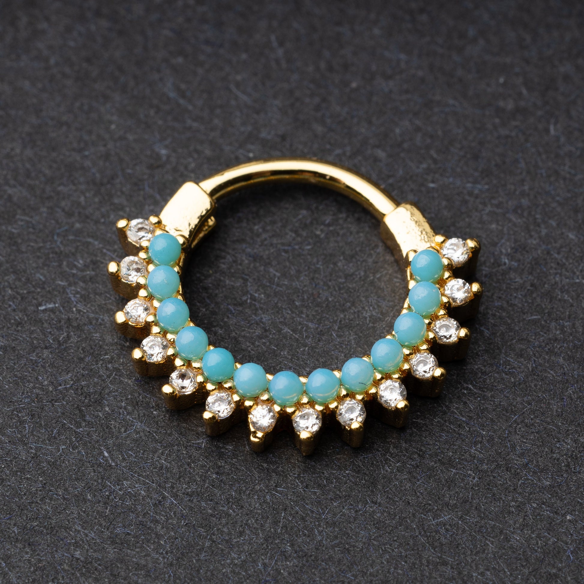 Gold-tone septum clicker with turquoise beads and cubic zirconia stones arranged in an elegant pattern, displayed on a dark background.
