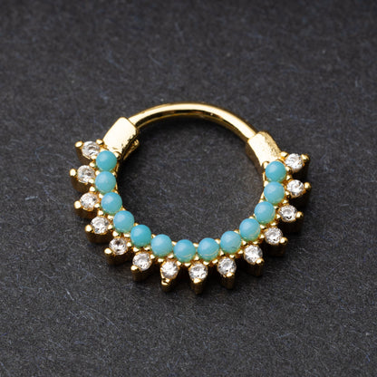 Gold-tone septum clicker with turquoise beads and cubic zirconia stones arranged in an elegant pattern, displayed on a dark background.