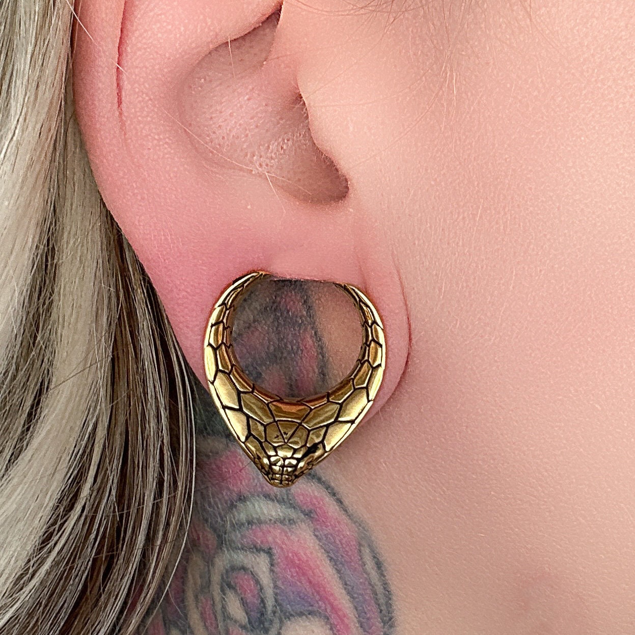 Snakehead saddle tunnel for stretched ears in gold displayed on a dark background.