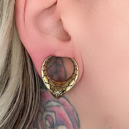 Snakehead saddle tunnel for stretched ears in gold displayed on a dark background.