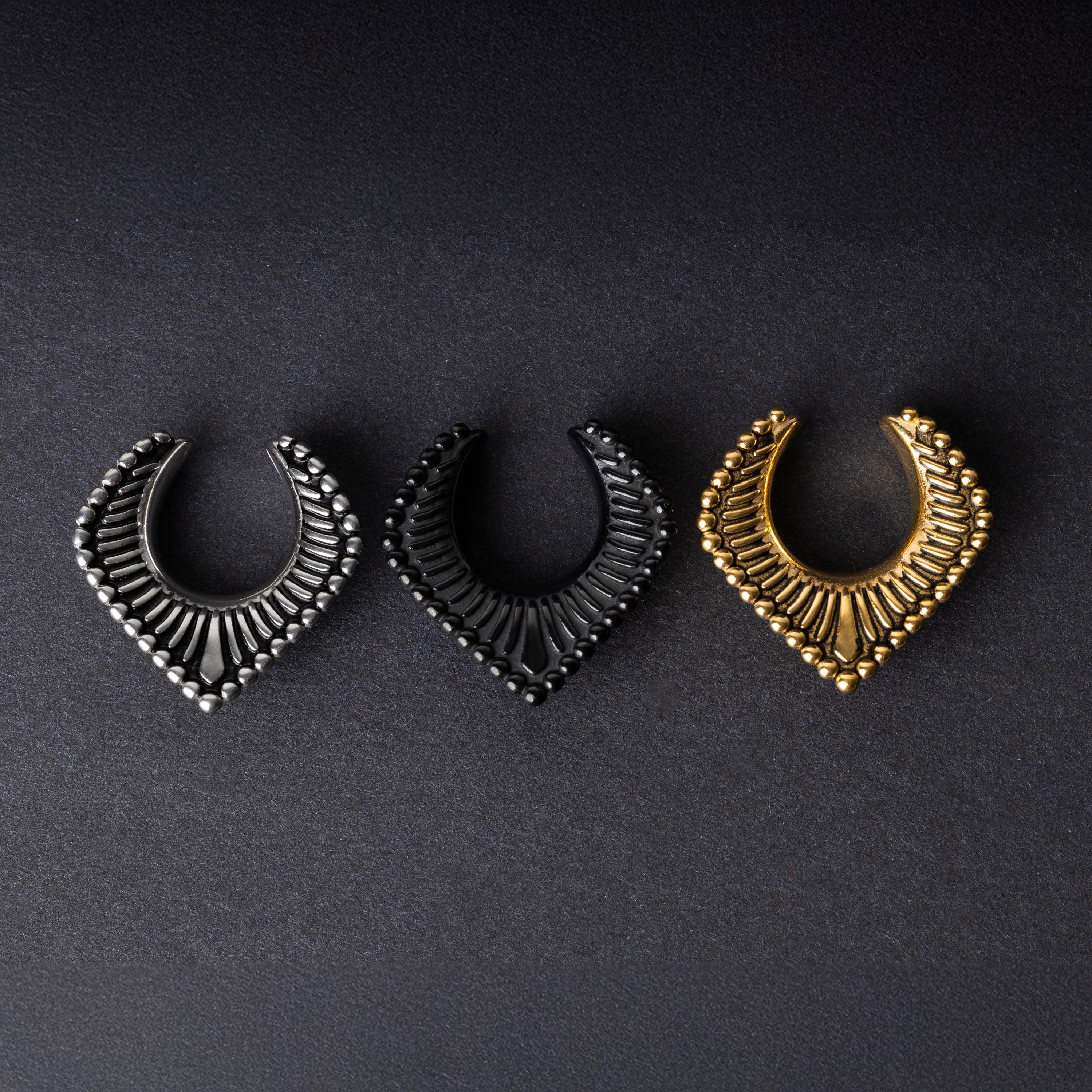 Three V-shaped stainless steel clickers in silver, black, and gold finishes arranged on a dark textured background.