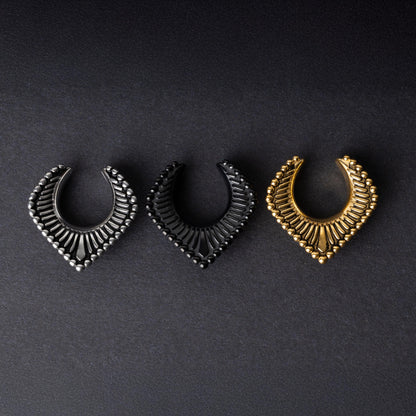 Three V-shaped stainless steel clickers in silver, black, and gold finishes arranged on a dark textured background.