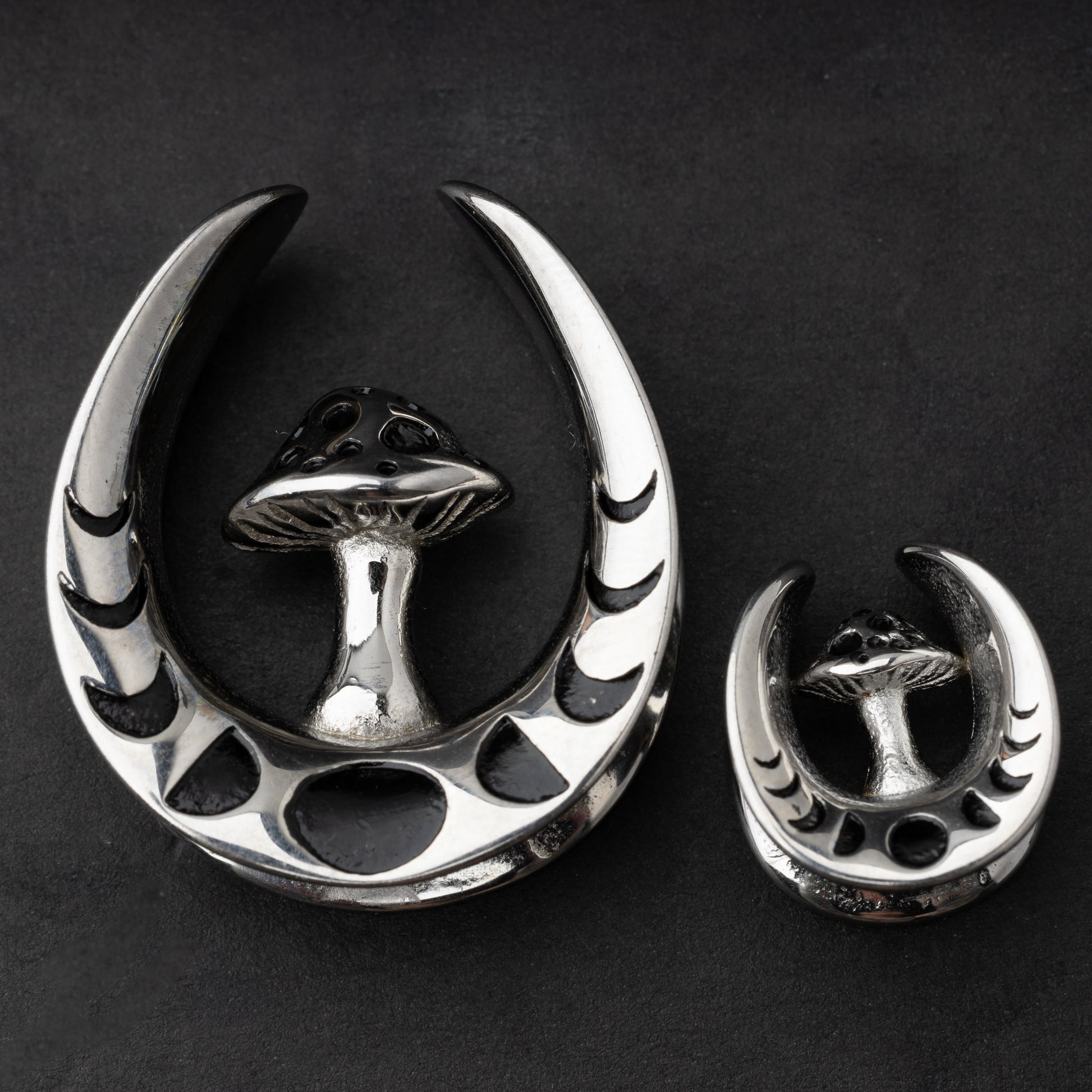 Pair of crescent moon tunnels with mushroom detailing in silver, displayed on a dark background.