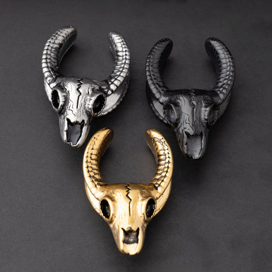 Three ram skull saddle tunnels in black, silver, and gold finishes, showcasing intricate skull details and bold design on a dark background.