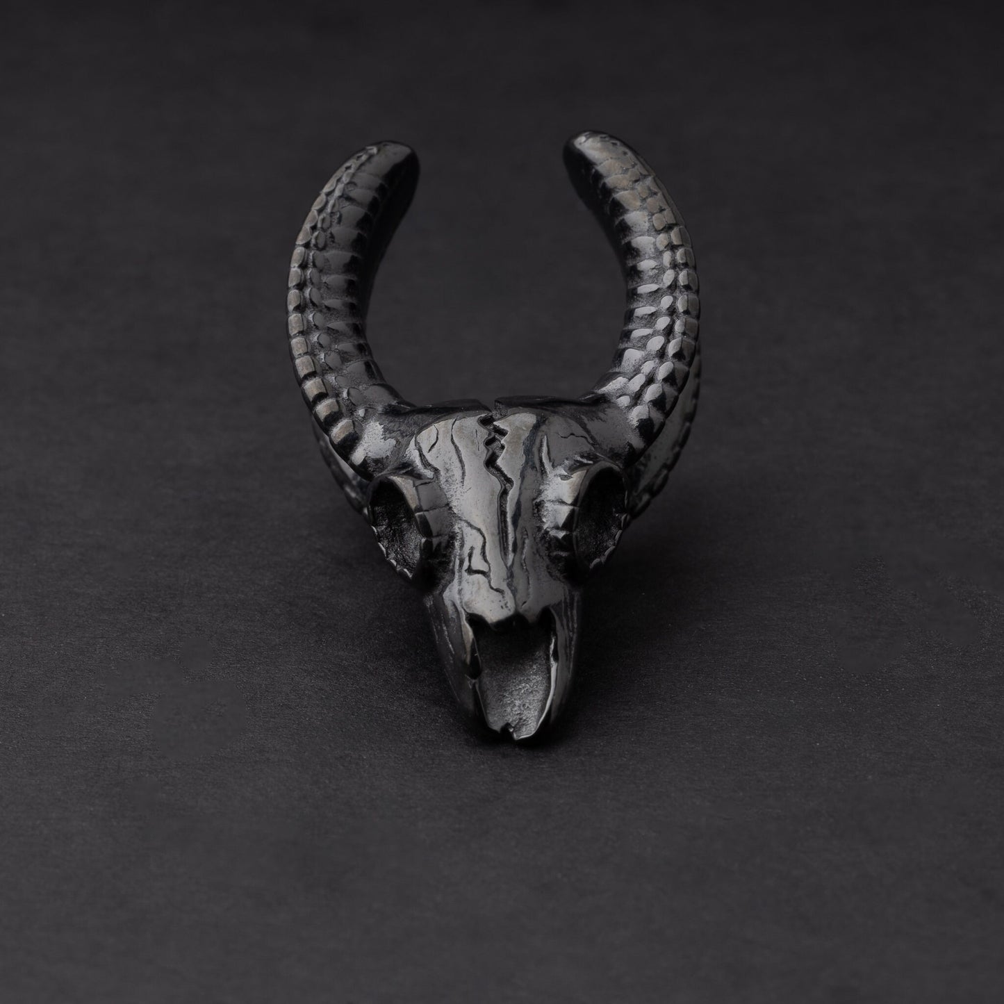 Ram skull saddle tunnel in black, showcasing intricate skull details and bold design on a dark background.