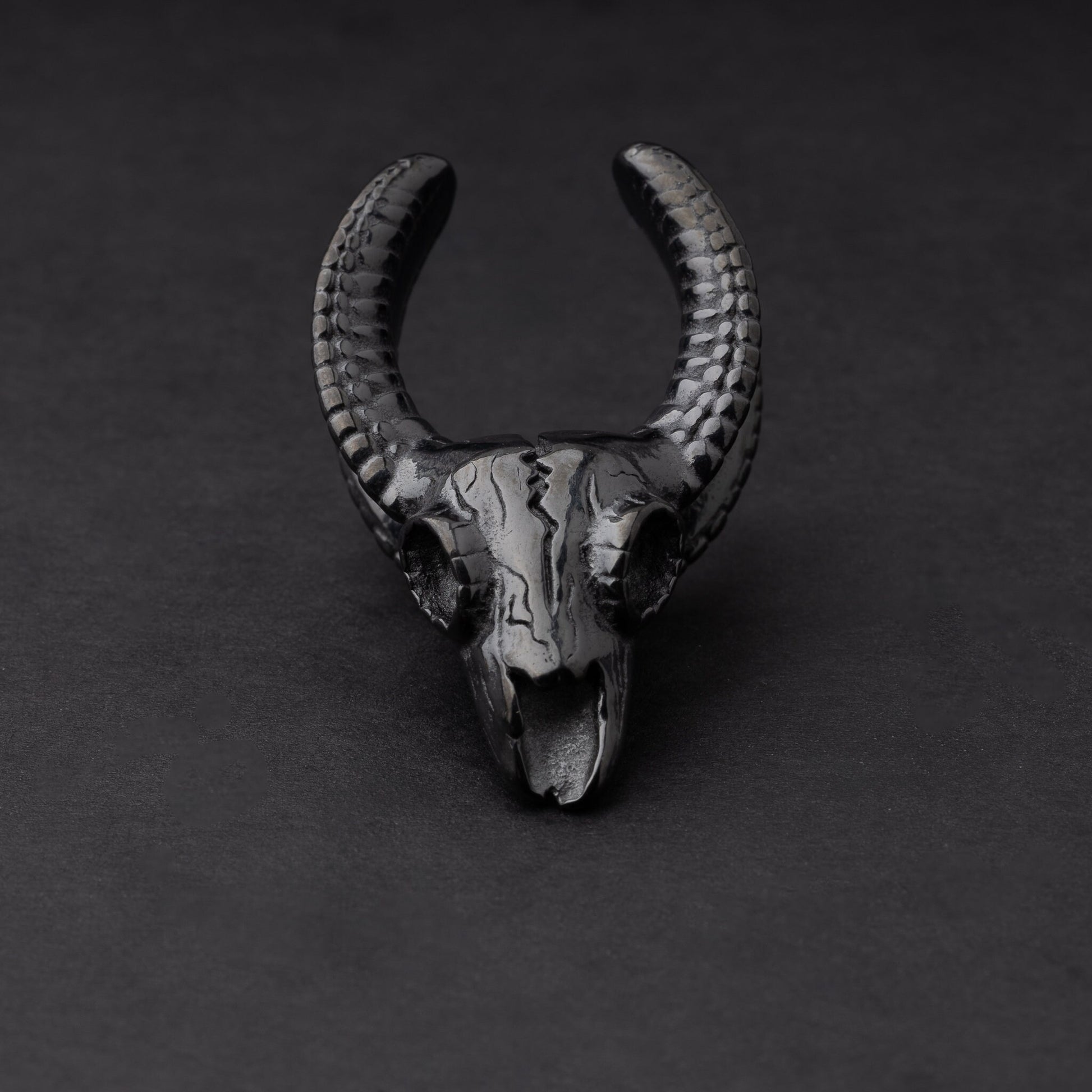 Ram skull saddle tunnel in black, showcasing intricate skull details and bold design on a dark background.