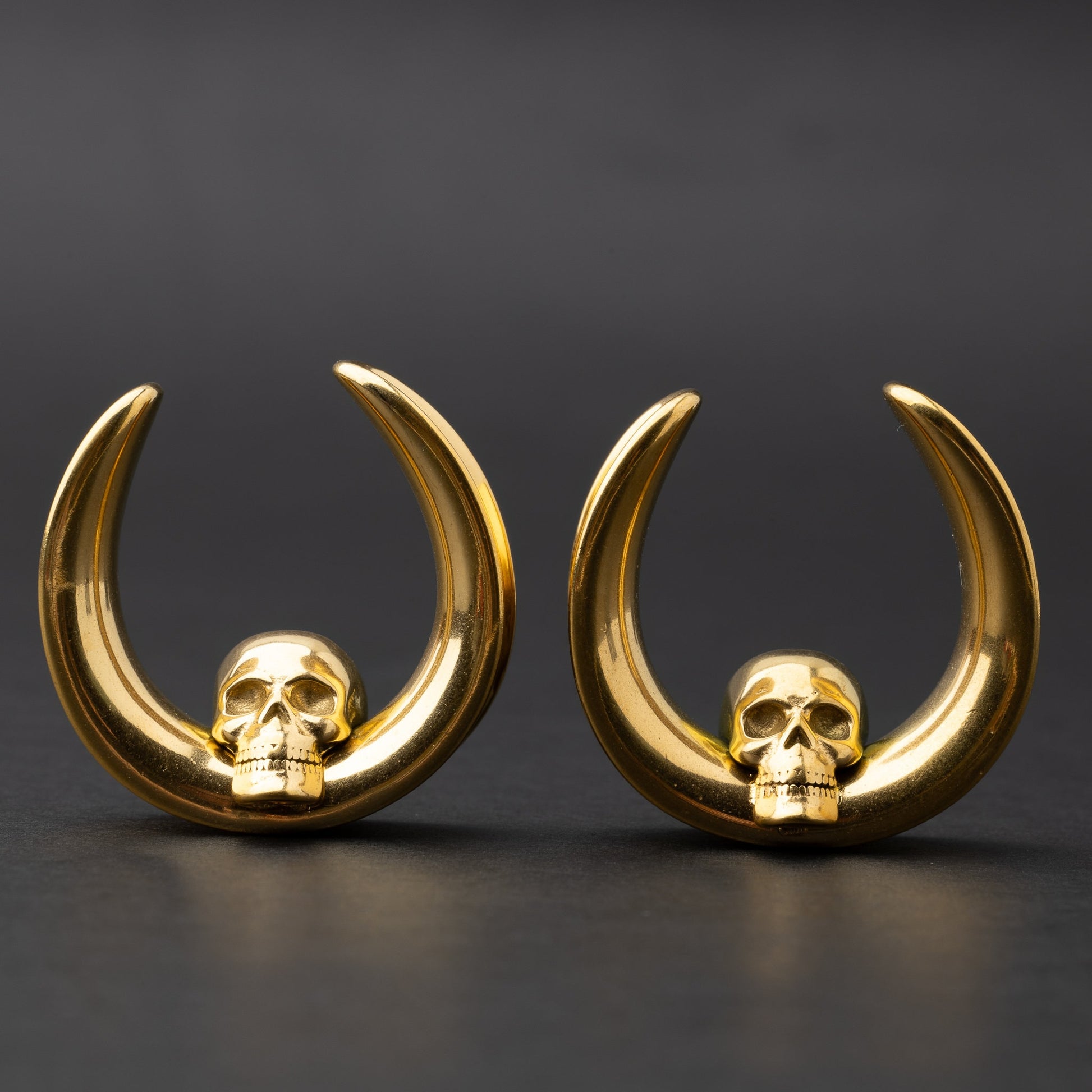 Pair of Skull design saddle tunnels in gold, displayed on a dark background.
