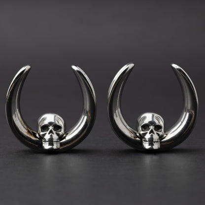 Pair of Skull design saddle tunnels in silver, displayed on a dark background.