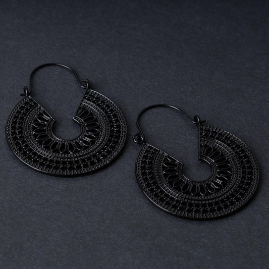 Pair of black hoop earrings with intricate cutout details and textured patterns, displayed on a dark background.