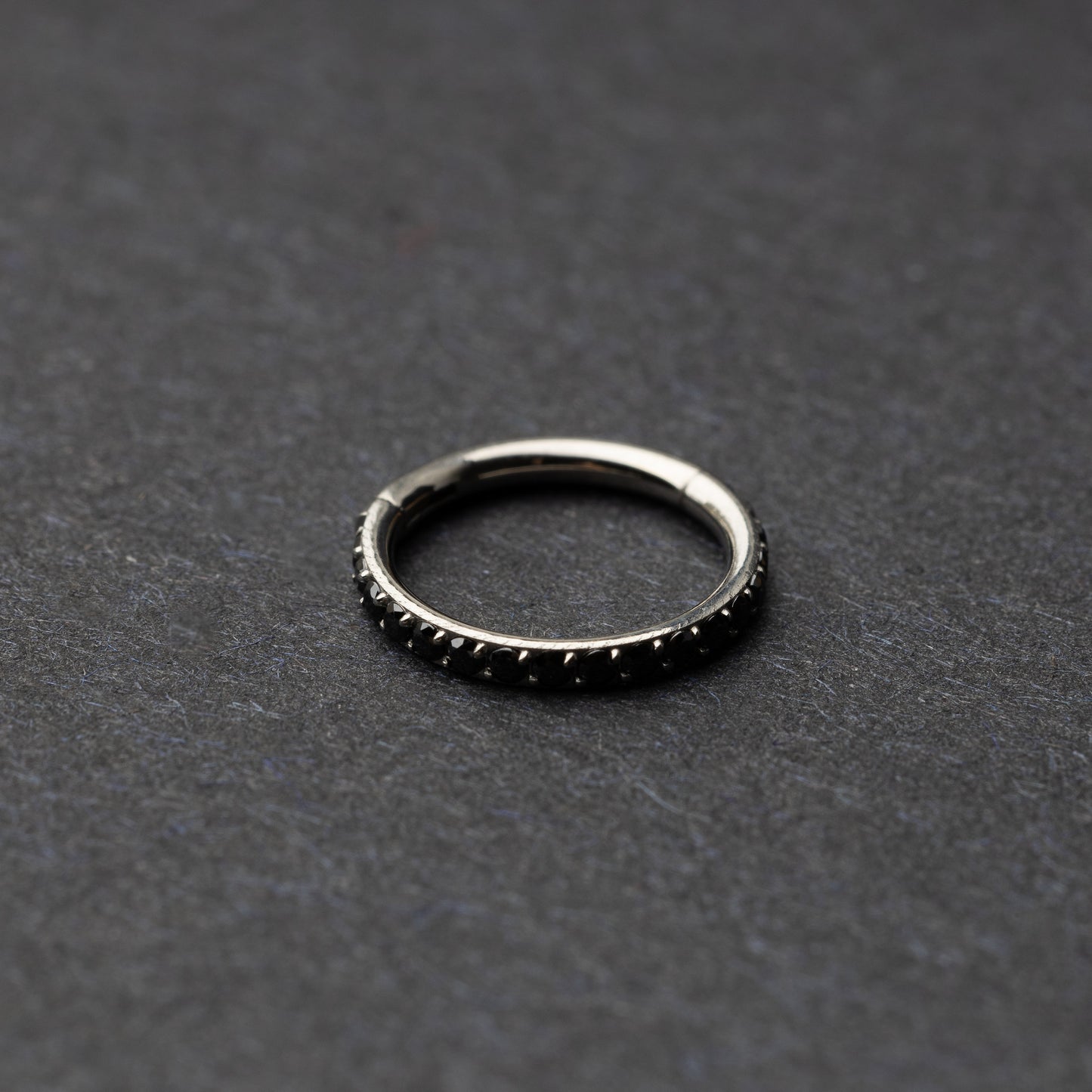 A textured stainless steel seamless ring with a polished finish, placed on a dark, textured background.