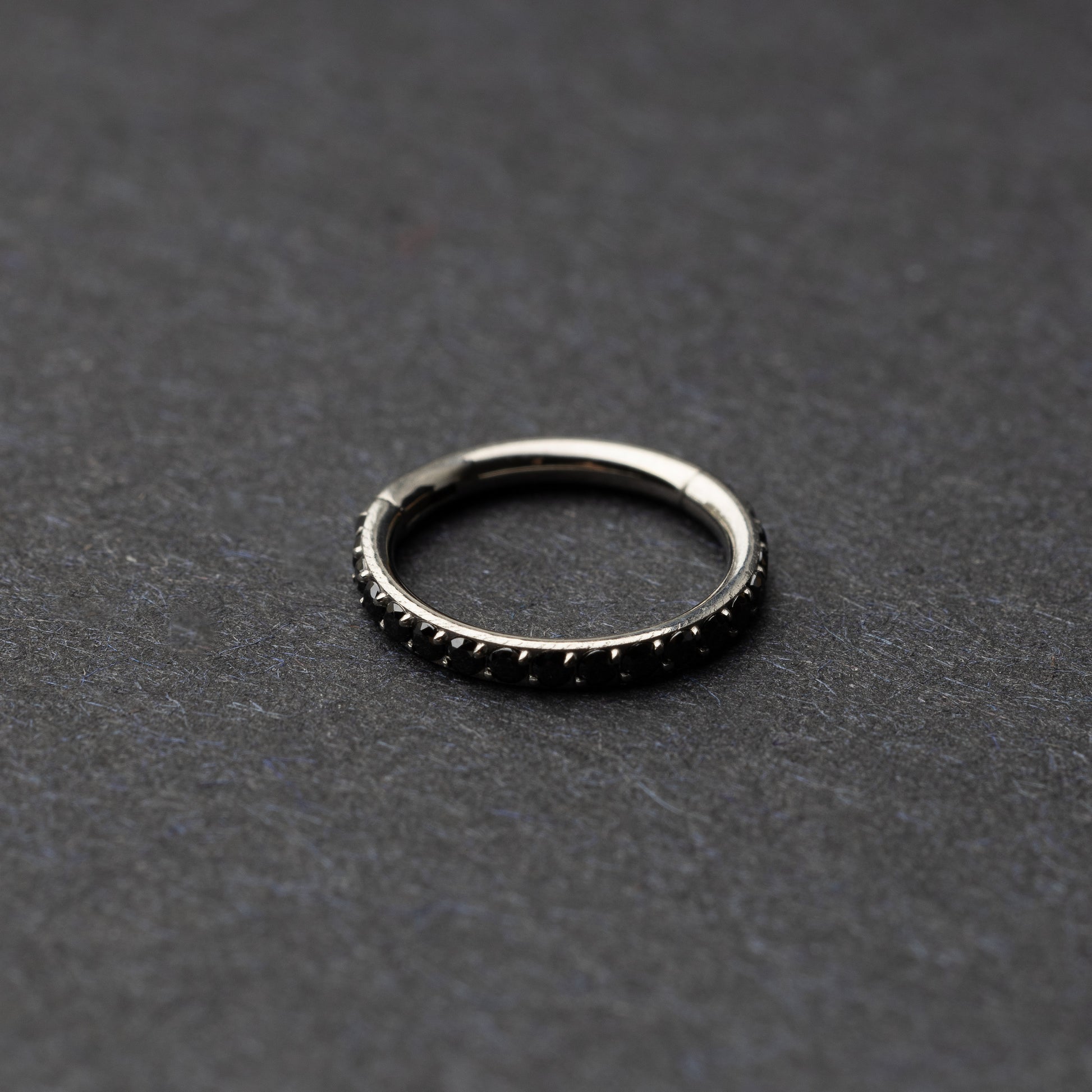 A textured stainless steel seamless ring with a polished finish, placed on a dark, textured background.