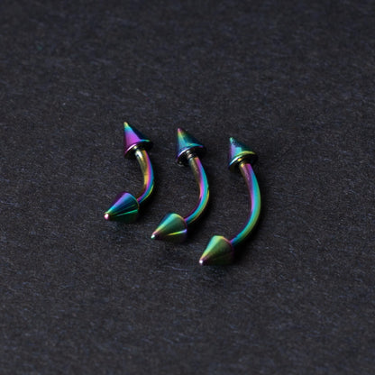 Three rainbow titanium curved barbells with cone-shaped ends, displayed on a dark textured background, showcasing their vivid color gradient and sleek design.