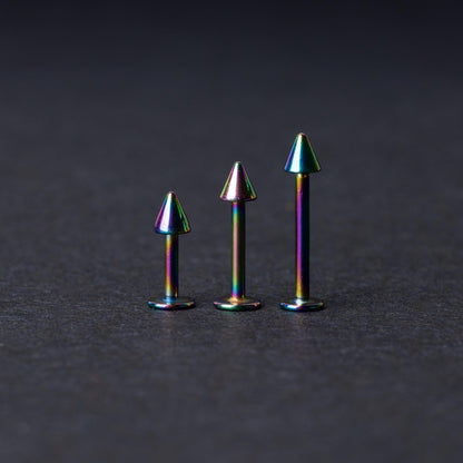 Three rainbow labret studs with cone-shaped tops displayed on a dark background, highlighting their iridescent finish and sleek, durable design.