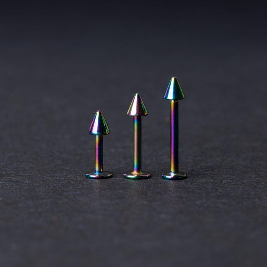 Three rainbow labret studs with cone-shaped tops displayed on a dark background, highlighting their iridescent finish and sleek, durable design.