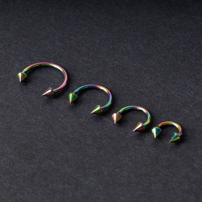 Titanium horseshoe hoops with spike ends, featuring a colorful rainbow finish, displayed on a dark textured background.