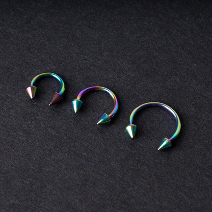 Three stainless steel horseshoe hoops with cone-shaped ends and a rainbow anodized finish displayed on a dark background, showcasing their bold design and vibrant colors.